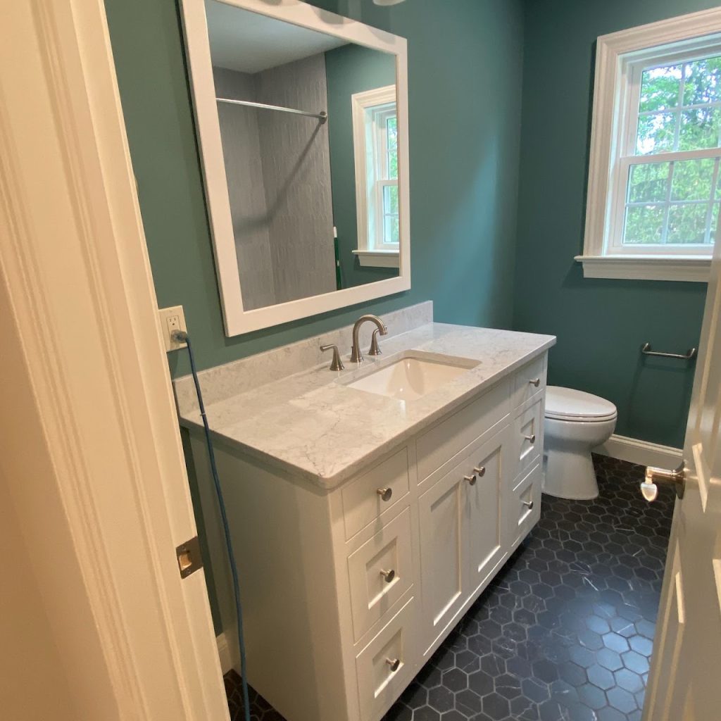 Completed blue bathroom with white vanity, dark hexagonal floor tile and toilet