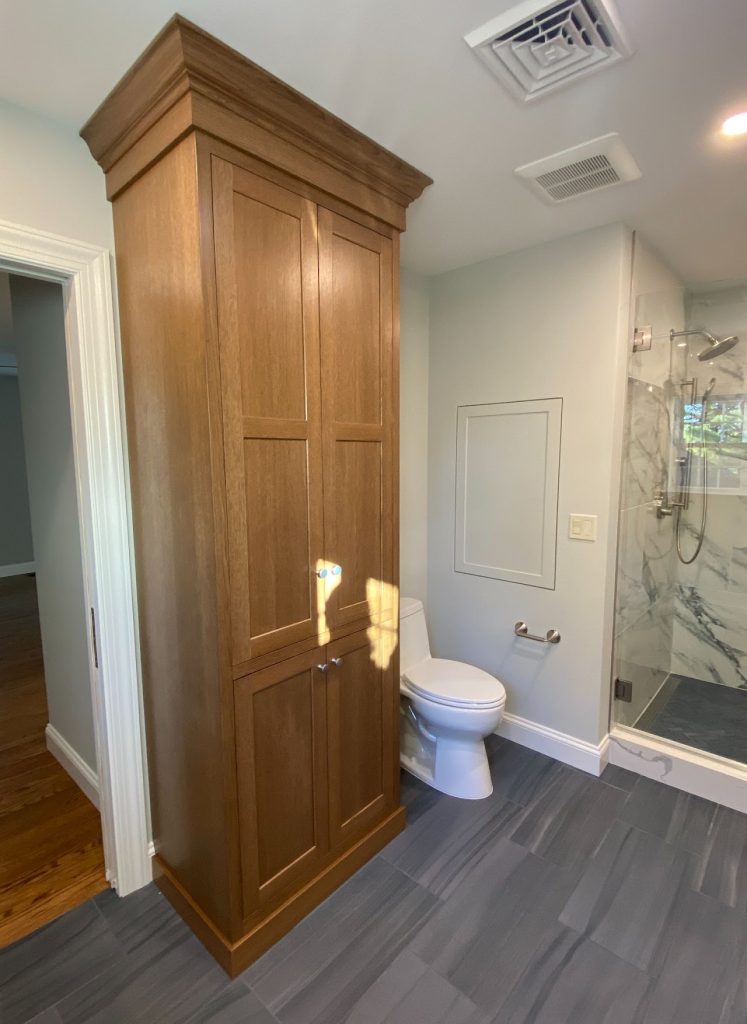 Completed main bathroom showing the tall wood cabinet, toilet and glass shower