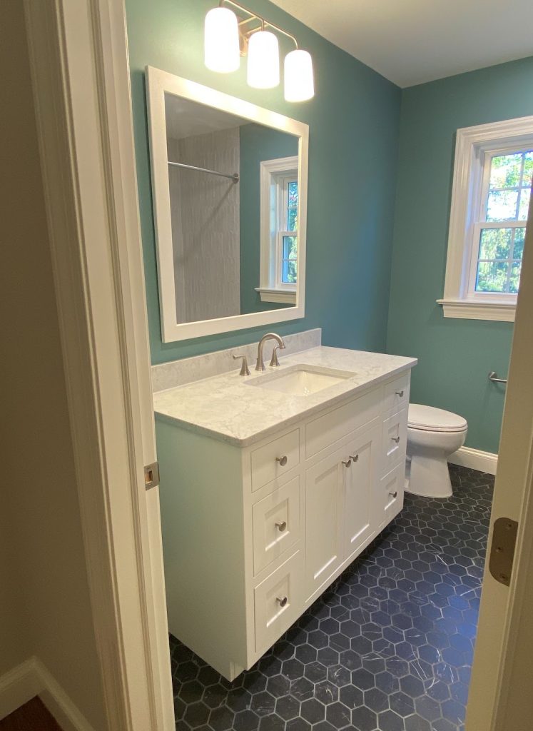Completed blue bathroom with illuminated mirror, white vanity and dark floor tile