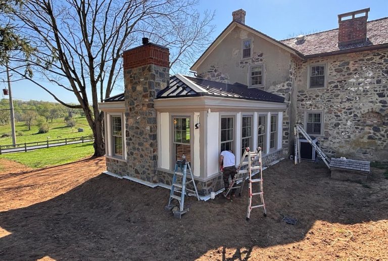 Completed sunroom addition with stone chimney, white siding and tall windows
