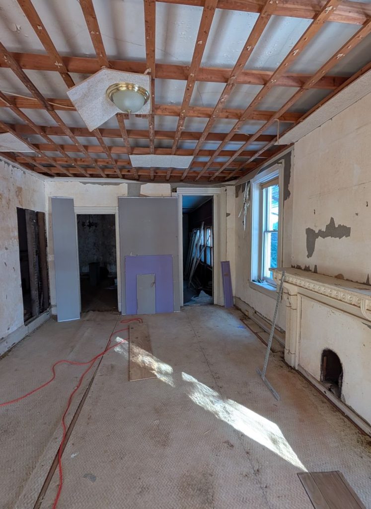 Existing room with exposed ceiling framing and damaged plaster before renovation